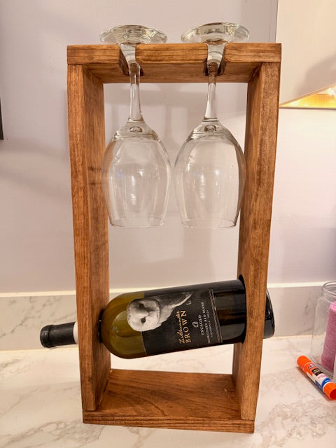 Wooden wine rack with a bottle and two glasses on a light-colored wall.