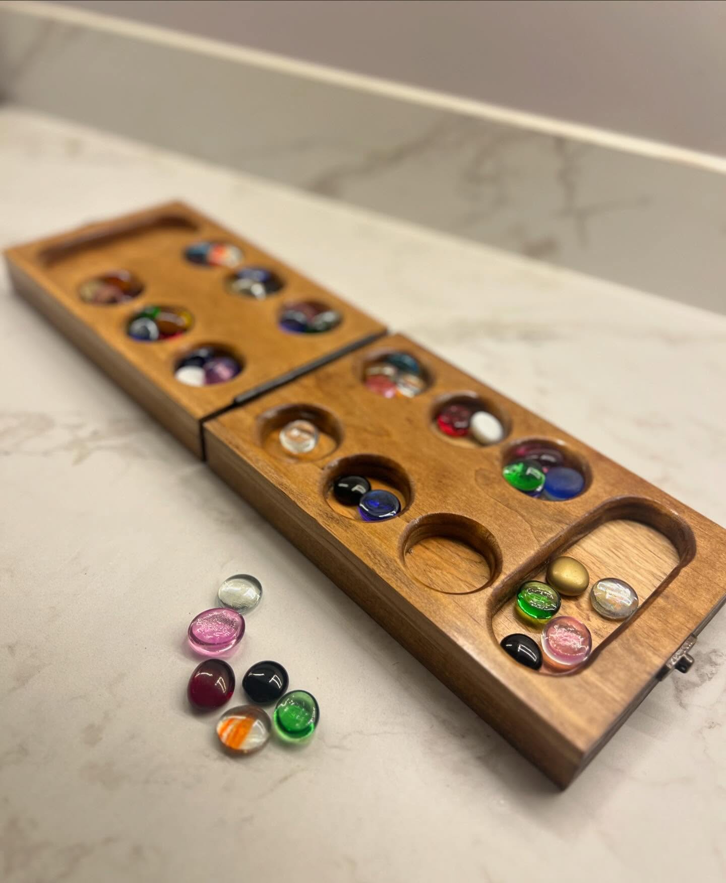 Wooden Mancala game set with colorful stones on a marble surface